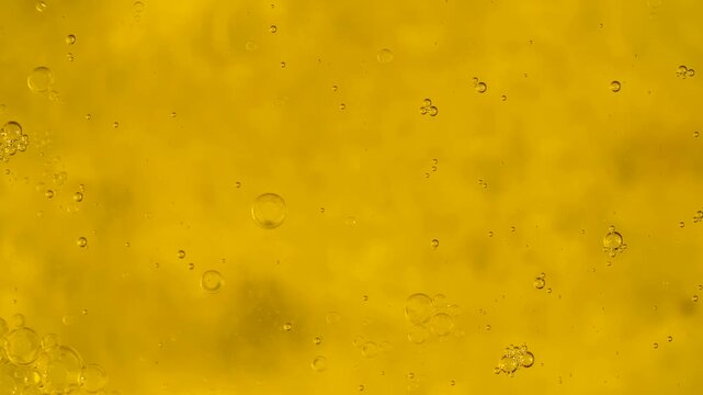 Top view of oil bubbles floating on the surface of water in a bright yellow macro background. Concept of food, cosmetic, science and abstract design use for packaging, branding and advertising.