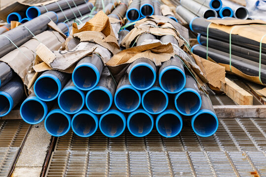 Industrial metal pipes with bright blue inner plastic lining stacked on steel drainage grates at construction site or port