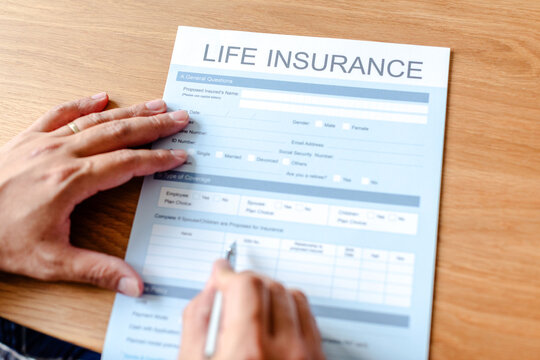 Person filling out a life insurance form on a wooden table.