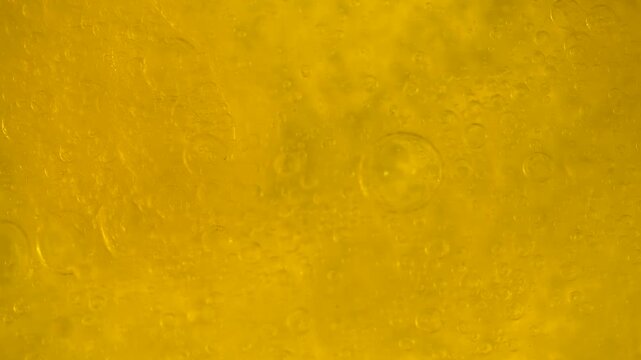 Top view of oil bubbles floating on the surface of water in a bright yellow macro background. Concept of food, cosmetic, science and abstract design use for packaging, branding and advertising.