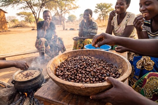 Zambian women sharing a traditional meal of roasted Bambara groundnuts from a wooden bowl