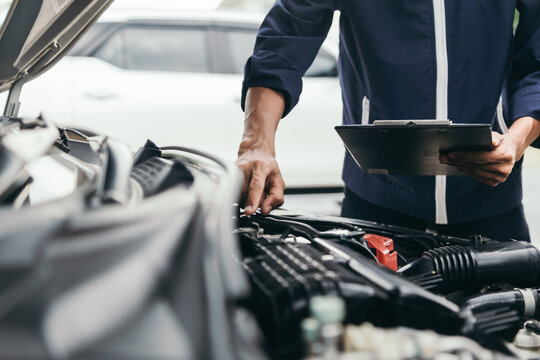Auto mechanic technician inspecting car engine with clipboard checklist.