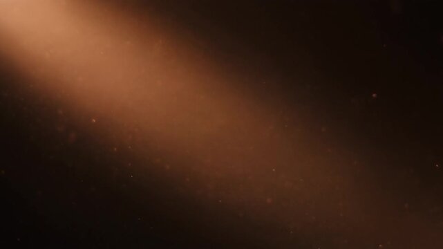 Warm copper dust drifts and swirls through diagonal backlight, particles catching soft glow against deep black with dreamy industrial atmosphere, cinematic depth, and gentle motion.