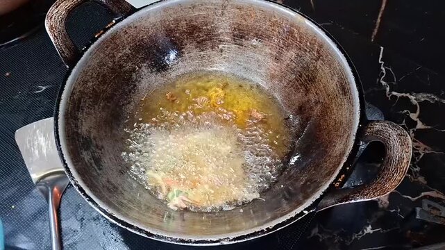 A person scoops vegetable batter into a traditional wok filled with hot oil to deep-fry crispy fritters.