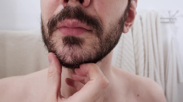 Man touching his mustache and beard, checking for new gray hairs and examining the skin underneath