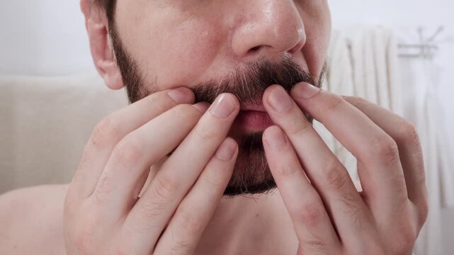 A man checks and separates his beard hairs, spotting gray strands appearing