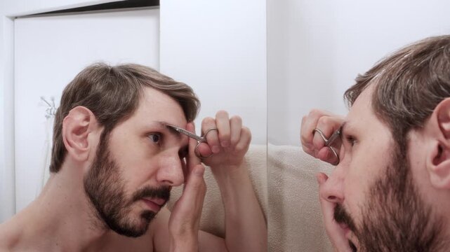 Man trimming his eyebrows with small scissors, carefully cutting individual long hairs