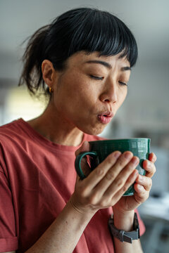 Asian woman blowing on hot morning tea