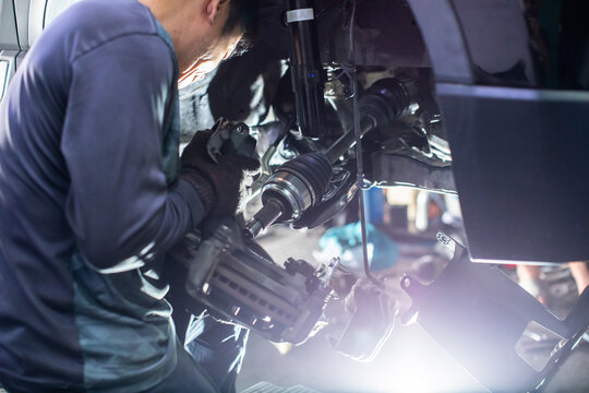 Selective focus to Professional car mechanic repairing front wheel suspension and brake system in an auto service garage. Concentrated technician working on drive shaft and vehicle components under br