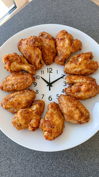 Golden-brown fried chicken wings creatively arranged to form a clock face on a white plate, featuring a central clock and hands, symbolizing mealtime, snack time, or the perfect moment for