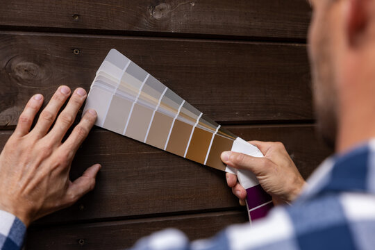 man choosing paint color from samples palette for wooden plank house exterior