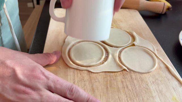 hands cutting circles out of rolled dough with a cup on a wooden board