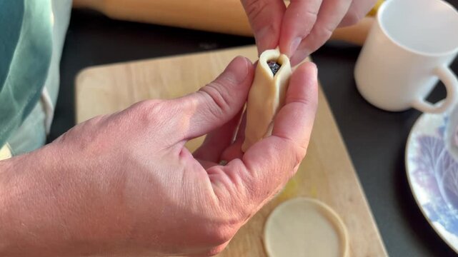 the cozy process of homemade cooking and baking. Hands shaping and sealing a dumpling with berry filling on a wooden board