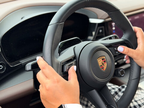 Hands holding a porsche steering wheel inside a luxury car interior, showing a modern dashboard and a driving view. porsche macan 4 electric Poland, Pszczyna, 3.08.2026
