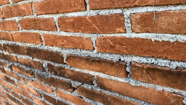 The texture of a red brick wall featuring a traditional brick arrangement and a rough cement mortar layer, showcasing surface details, patterns, and material character.