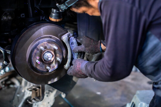 Motion blur picture of a mechanic wearing headlamp and gloves replacing brake pads on a car disc brake system in an auto repair workshop.