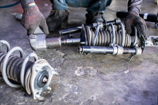 selective focus to mechanic in protective gloves using a pneumatic tool and spring compressor to repair a car shock absorber assembly on a garage floor.