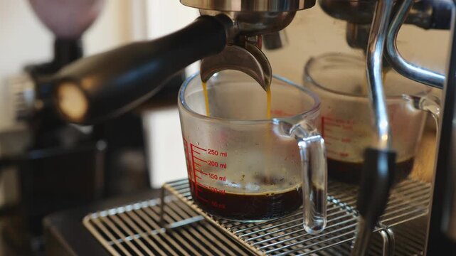 Close-up of espresso being extracted from a coffee machine portafilter into a glass measuring cup, dark golden crema streaming down, precise coffee brewing process for quality control.