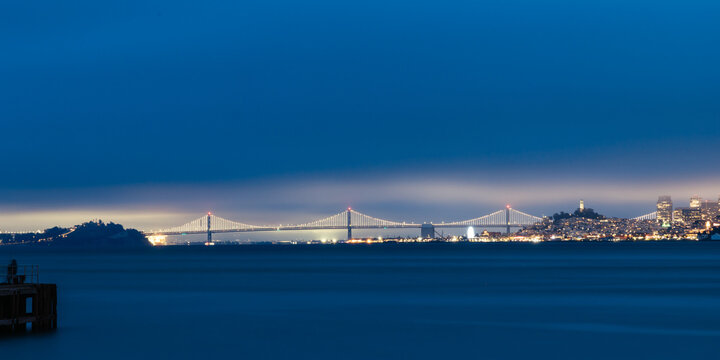 Illuminated San Francisco Oakland Bay Bridge at night from a wooden pier