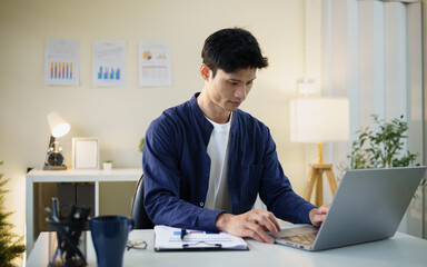 Fototapeta premium Young Asian businessman reviewing reports and planning work at his office desk.