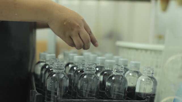 Hand inspecting rows of sealed drinking water bottles on a manual production line in a small-scale water bottling factory, workers checking quality before packaging, local water bottling small busines