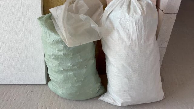 Green and white woven polypropylene sacks standing on a concrete floor at a construction site