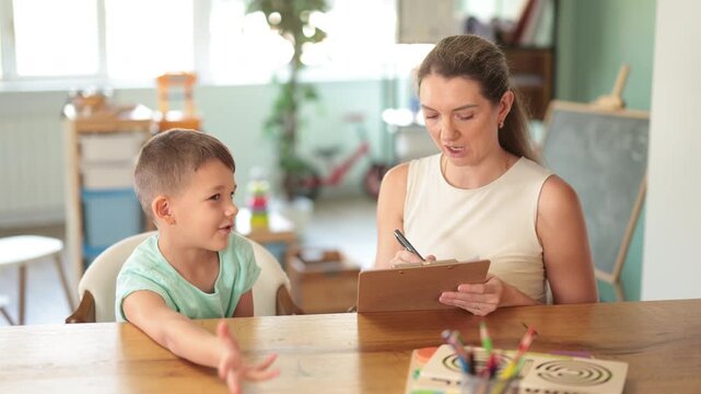 Child psychologist fills out questionnaire and interviews boy in a kindergarten. High quality 4k footage