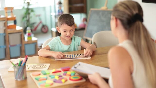 Focused little boy tracing wooden labyrinths with both hands during psychological test at development center