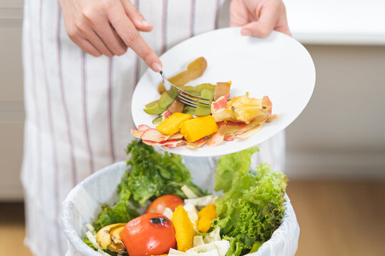 Compost from leftover food asian housekeeper woman hand holding peel plate use fork scraping waste, rotten vegetable throwing away into garbage, trash or bin. Environmentally responsible concept.
