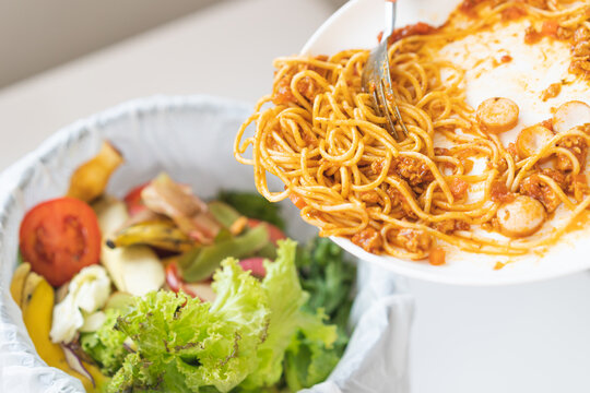 Compost from leftover food asian young housekeeper woman, female hand holding spaghetti plate use fork scraping waste, food throwing away into garbage, trash or bin. Environmentally responsible.