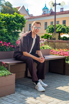 young handsome guy in brown clothes sits on a wooden bench in a busy city square.