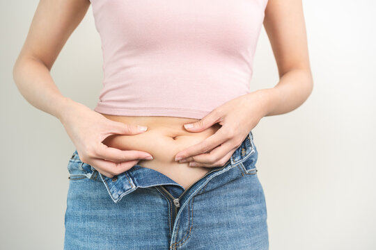 Weight gain, overweight, high cholesterol and pressure, woman hand pinching excess fat big belly with finger and wear tight trousers, show fat around abdomen body, getting loss, isolated on background