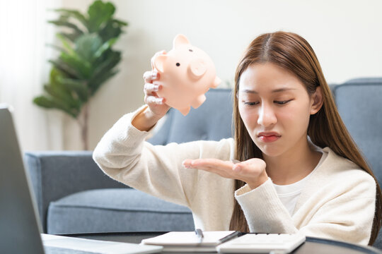 Finance person concept, asian young woman, girl emptied her piggy bank to use her savings but there wasn't enough money when sitting in living room at home, financial plans to spend enough money.