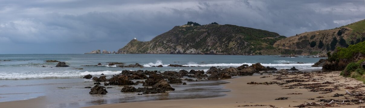 Nugget Point Lighthouse auf schmalem Felsgrat mit Blick auf die Nuggets-Felsen und schwachem Regenbogen, Otago, Neuseeland