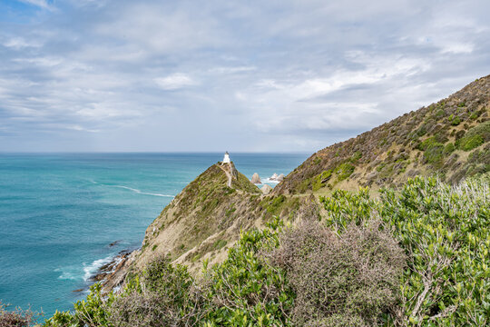 Nugget Point Lighthouse auf schmalem Felsgrat mit Blick auf die Nuggets-Felsen und schwachem Regenbogen, Otago, Neuseeland