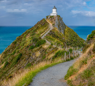 Nugget Point Lighthouse auf schmalem Felsgrat mit Blick auf die Nuggets-Felsen und schwachem Regenbogen, Otago, Neuseeland