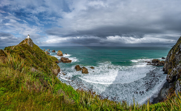 Nugget Point Lighthouse auf schmalem Felsgrat mit Blick auf die Nuggets-Felsen und schwachem Regenbogen, Otago, Neuseeland