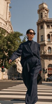 Stylish person in oversized navy suit and sunglasses walking across a city intersection for street style background and contemporary fashion imagery
