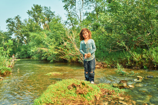 Boy standing in a river holding a dripping clump of mud and grass