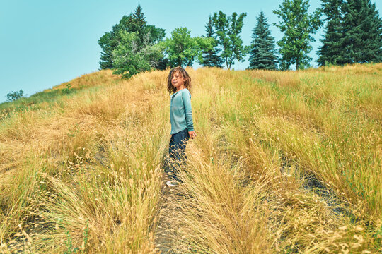 Boy standing on a hillside path in tall grass looking back
