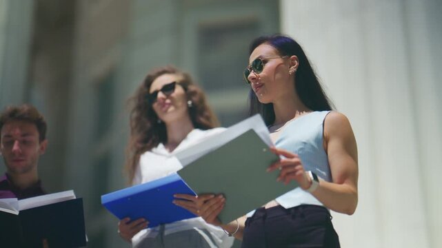 Three young business people are focused on reviewing important documents outside. They are collaborating on a project in a bright outdoor urban setting.