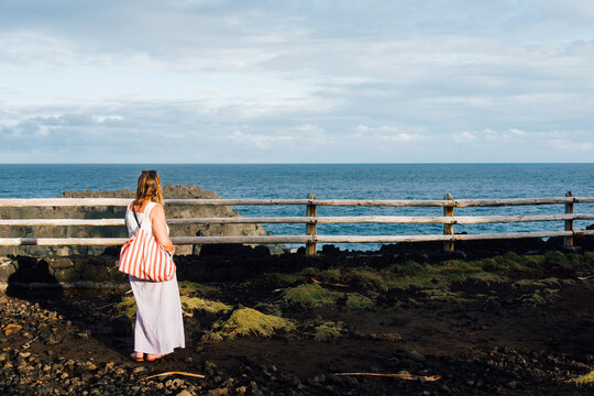 Femme regardant la mer. Vacanci&egrave;re contemplant l'horizon le soir au bord l'Oc&eacute;an Indien. Seule face &agrave; la mer. Touriste avec un sac rouge &agrave; La R&eacute;union