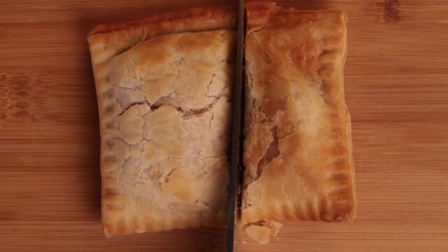 Cutting a Sausage, Bean and Cheese Pasty in Half on a Chopping Board Top-Down View