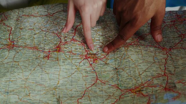 Two pairs of hands (a man's and a woman's) are pointing to and tracing a location on a paper road map (focusing on the Hannover area and its surroundings in Germany).