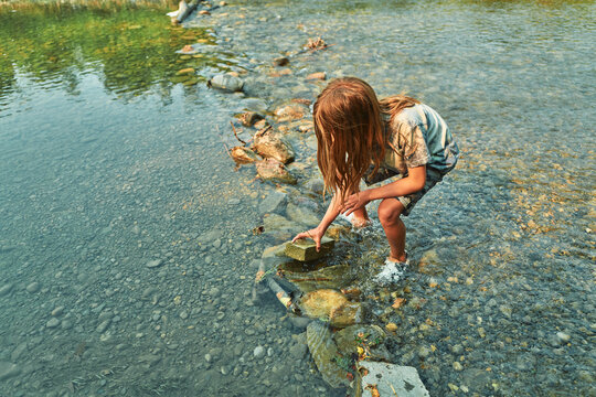Boy crouching at the edge of a shallow river stacking rocks