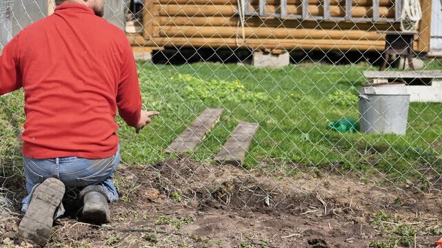 A man is unrolling the wire for a chain-link fence on his plot.