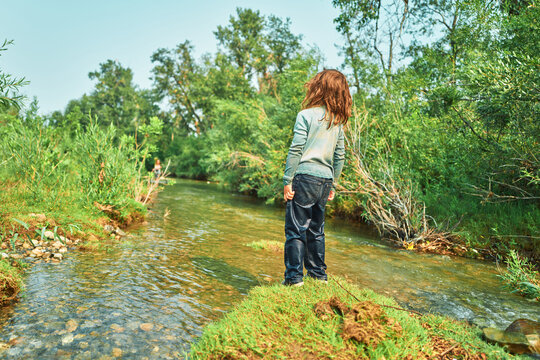 Boy standing on a grassy riverbank looking downstream