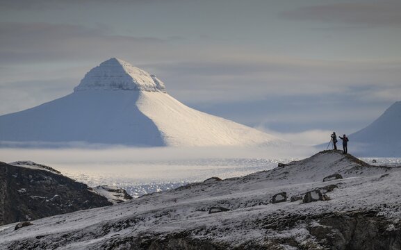 Two people, including a photographer with a stand in front of one of the three mountains Tee Kroner, Kongsfjord or Kongsfjorden, Spitsbergen archipelago, Svalbard, Norway