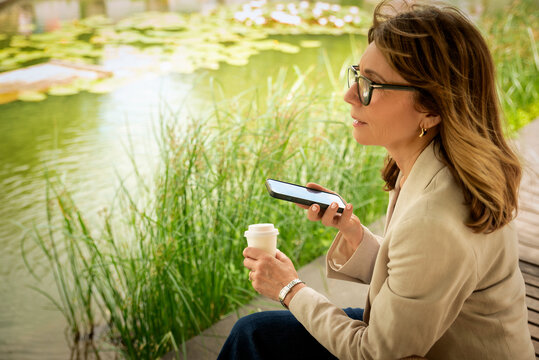 Confident mid-aged woman sitting in a city park and using a cell phone