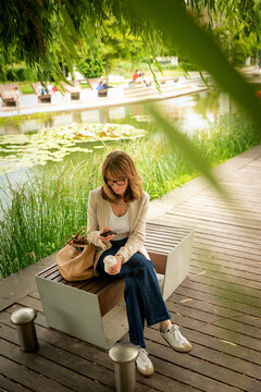 Confident mid-aged woman sitting in a city park and using a cell phone